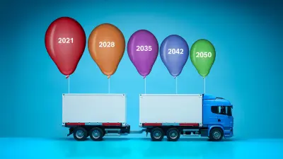 A toy truck with five multicolored and different sized balloons attached to its roof, marked with years ranging from 2021 to 2050