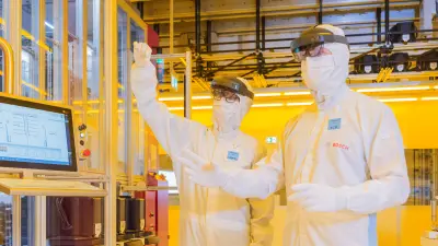 Two associates standing in the fab in white protective gear use VR glasses and a monitor for maintenance work.