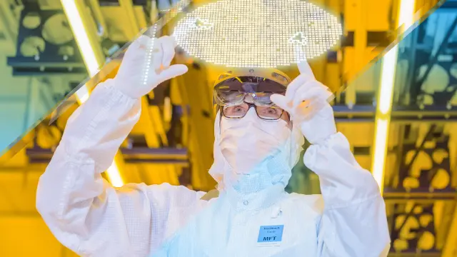 Eine Person in weißem Schutzanzug blickt durch eine AR-Brille auf das Hologramm eines Wafers.