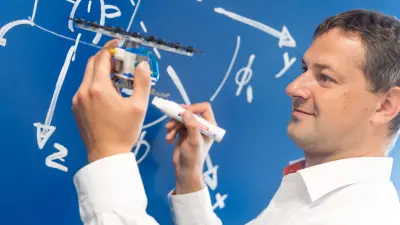 Marcus Parentis with a smal model of a flying taxi. He writes some calculations on a blackboard.
