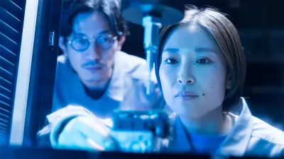 Two people are closely observing a piece of equipment under blue lighting.