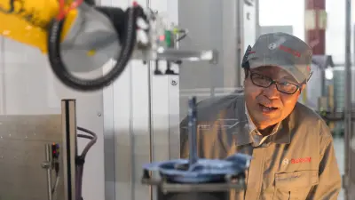 Eine Person in Bosch-Uniform steht neben einer industriellen Maschinen, einschließlich eines Roboterarms.