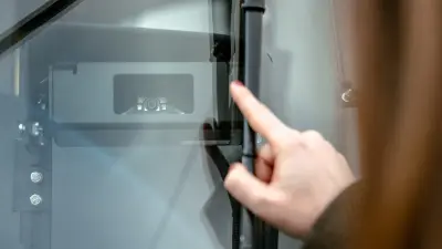 Ein Finger zeigt auf eine Kamera des Fahrassistenzsystems, das hinter der Frontscheibe einer Straßenbahn angebracht ist.
