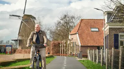 Der Bosch-Mitarbeiter Gert Brommer fährt auf seinem Fahrrad einen Damm in Holland entlang. Im Hintergrund ist eine historische Windmühle zu sehen.