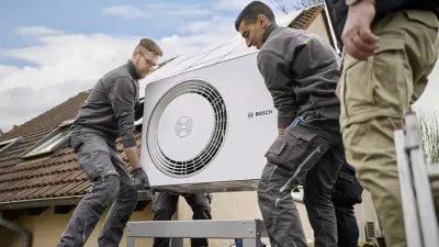 Vier Männer heben eine Bosch-Wärmepumpe bei der Installation auf ein vorbereitetes Chassis.