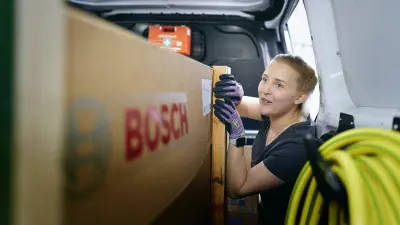 Eine Frau sichert eine verpackte Bosch-Wärmepumpe in einem Transporter für die Fahrt.