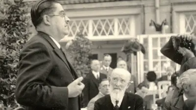 Robert Bosch sitting at a table with other people, looking at the speaker standing to his left.