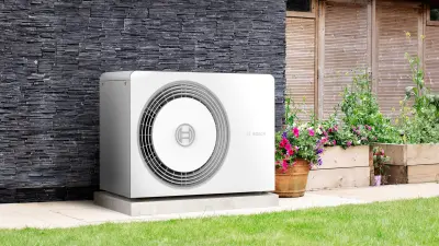 A Bosch air-water heat pump stands on the corner of a house in the front yard.