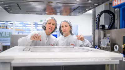 Two people in white lab coats and hairnets are inspecting a large industrial machine.
