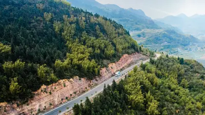 A truck winds down a lonely road through verdant forested mountains.