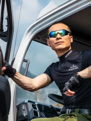 A man wearing a black T-shirt and sunglasses sits in the driver’s cab, holding the door open and looking back past the photographer.