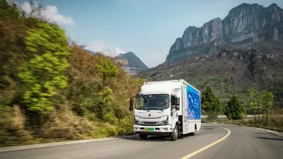 A truck traveling fast on a two-lane highway, shot at an angle from the front left. A mountain panorama provides the backdrop.