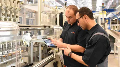 Two Bosch associates are standing in a factory and are monitoring the processes using a tablet.