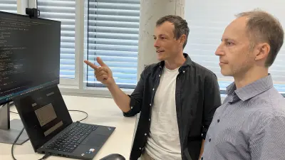 Two people reviewing code and data on computer screens