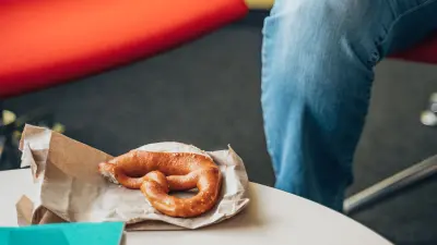 Pretzel on a paper bag on a table next to a seated person