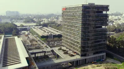An aerial shot from a high vantage point captures a sprawling cityscape under a hazy sky, centered on a modern, multi-story building prominently displaying the red "BOSCH" logo in local language on its upper facade.