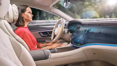 A woman is driving leisurely in a futuristic car. She isn't holding the steering wheel.