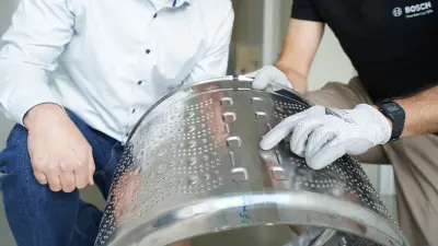 Specialists inspect a perforated metal component and examine a weld seam.