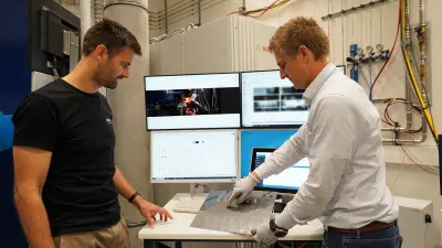 Peter Stritt (left) and Philipp Krüger (right) analyze a metal sample at a test station with multiple monitors.