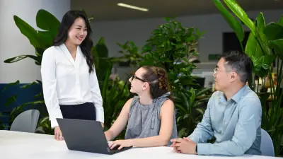 Jessica steht neben zwei Kollegen und lächelt sie an.