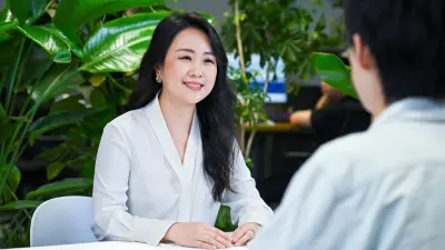 Jessica sitzt gegenüber ihres Mitarbeiters und lächelt ihn an.