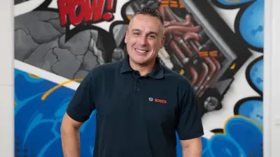 Mario steht vor einer farbigen Wand und lächelt in die Kamera.