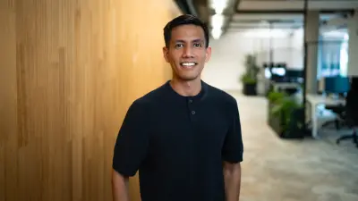 Antonio wears a black shirt, stands in an offi ce and smiles at the camera.