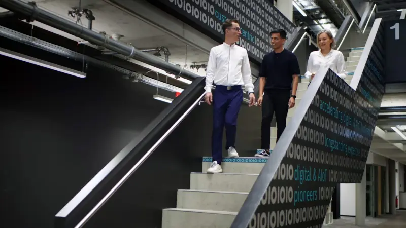 Hamza, Antonio and Karolina walk down a staircase and chat.