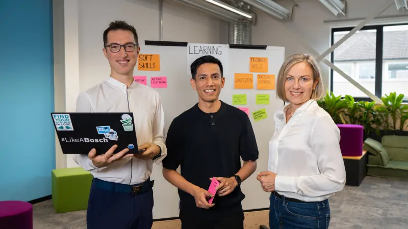 Hamza, Antonio and Karolina stand in front of a workshop board covered with sticky notes.
