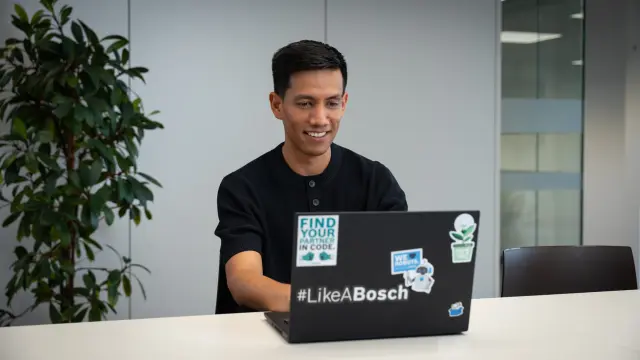 Antonio trägt ein schwarzes Shirt, steht in einem Büro und lächelt in die Kamera.