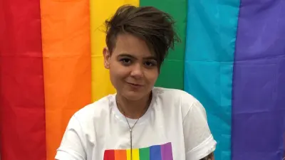 Bosch-Mitarbeiterin Caroline Benson lächelt in die Kamera und sitzt vor einer Regenbogenfahne.