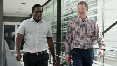 Two men walk over a bridge in a building.