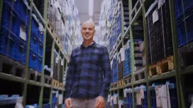 Benjamin stands between two high shelves and looks upwards while the camera pans around him.