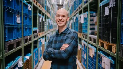 Benjamin stands with his arms folded between two high shelves and smiles at the camera.
