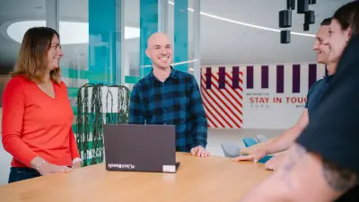 Benjamin has a meeting with his team at a high table and looks round with a smile.