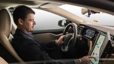 Projektleiter Michael Fausten betrachtet sein Spiegelbild in der Seitenscheibe eines Testfahrzeugs der Marke Tesla.