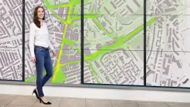 Dr. Maria Martínez Prada stands next to a wall-covering map that shows the air quality around Brixton Road.