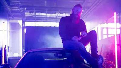 In einer Halle sitzt der Weltmeister im Handy-Rennspiel „Asphalt 9“ Florian Roschu auf einem Auto, das Smartphone in der Hand. Die Szenerie ist neblig und wird von einer pinkfarbenen Neonröhre beleuchtet.
