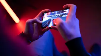 Ein Mann hält ein Smartphone. Auf dem Display ist eine Spielszene mit einem roten Sportwagen aus dem Handy-Spiel „Asphalt 9“ zu sehen.