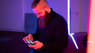 Der Weltmeister im Handy-Rennspiel „Asphalt 9“ Florian Roschu lehnt an einem Auto und spielt das Rennspiel auf seinem Smartphone. 