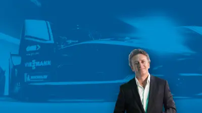 Alejandro Agag, Vorsitzender der Formel E, vor einem Hintergrund, der einen Rennwagen der Formel E zeigt.