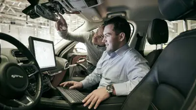 Andreas Schulz and Matthias Birk use a computer to adapt the system directly in the cockpit of the test car for automated driving.