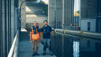 Two people wearing safety vests stand beside a water basin within a large concrete structure.