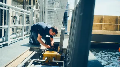 Person kneeling beside hydraulic machinery and pipes at the edge of a water basin