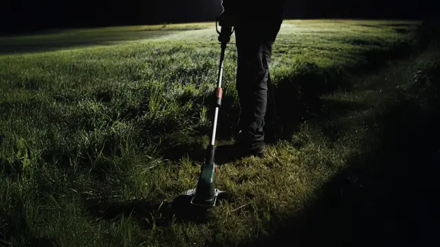 Once again the man at night, operating the Bosch UniversalGrassCut garden tool to cut the grass with precision. The tool is equipped with a telescopic handle for ergonomic use.