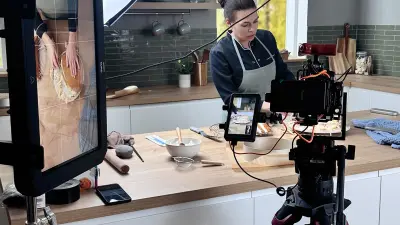 We see Dominique at work while a camera records her hands. On the left of the picture is a digital screen on which her work is visible.
