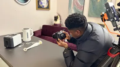 The cameraman takes a picture of the three kitchen appliances (hand mixer, toaster, kettle) You can't tell which one is the cake.