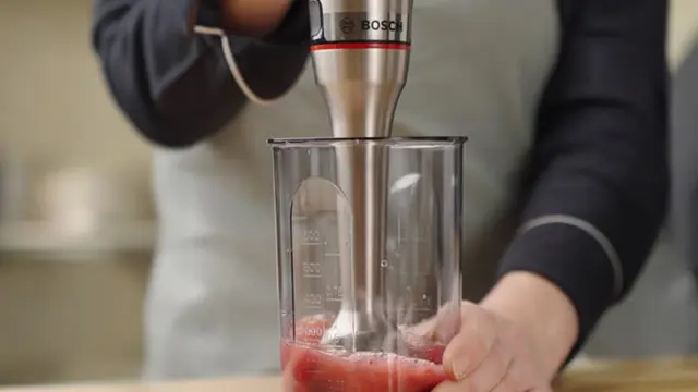 A woman in the cut operates a blender and uses it to puree berries to a liquid consistency.