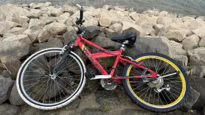 Rotes, sauberes Fahrrad liegt auf Felsen am Wasser.