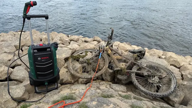 Dreckiges Fahrrad liegt am Rhein neben einem Hochdruckreiniger. 